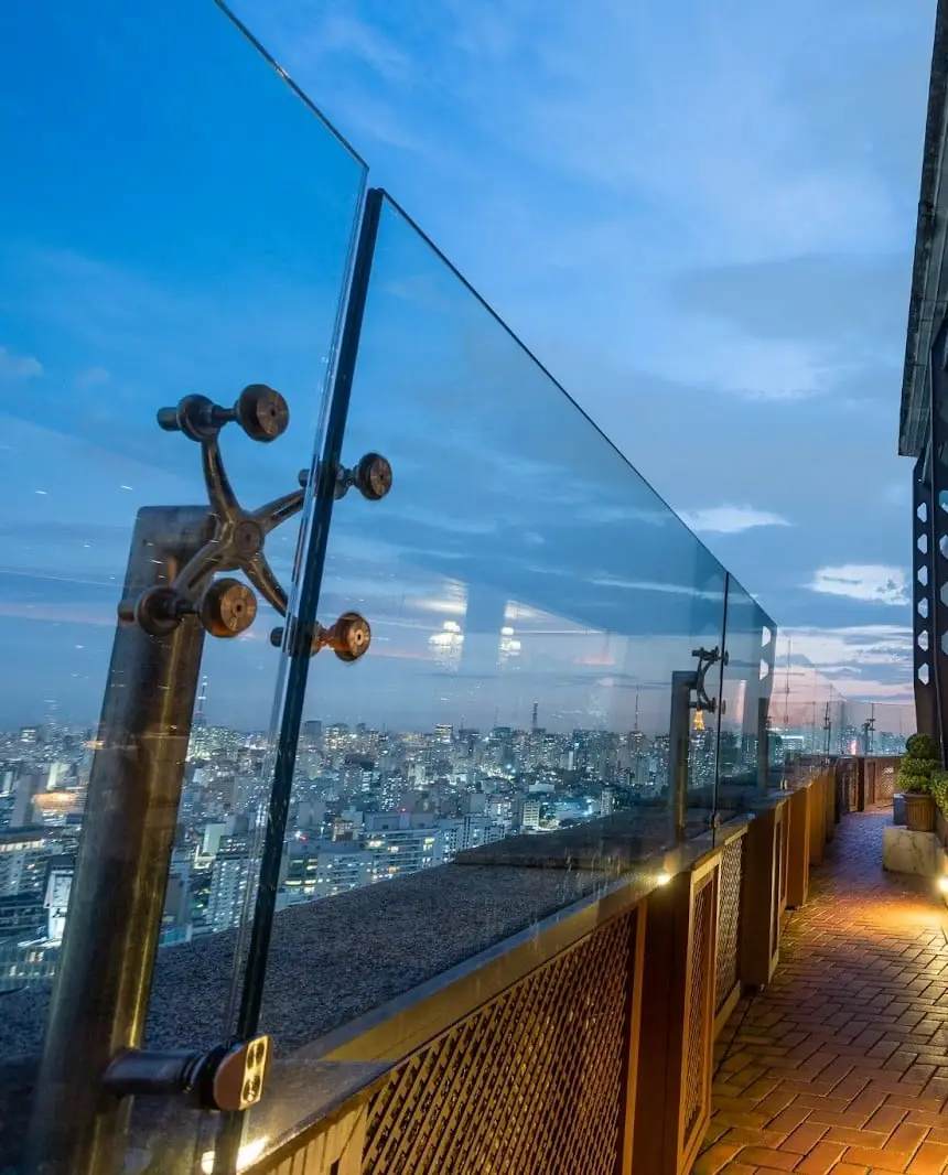 O mirante do Terraço Itália ao entardecer: o parapeito de vidro, o caminho iluminado e a cidade de São Paulo ao fundo